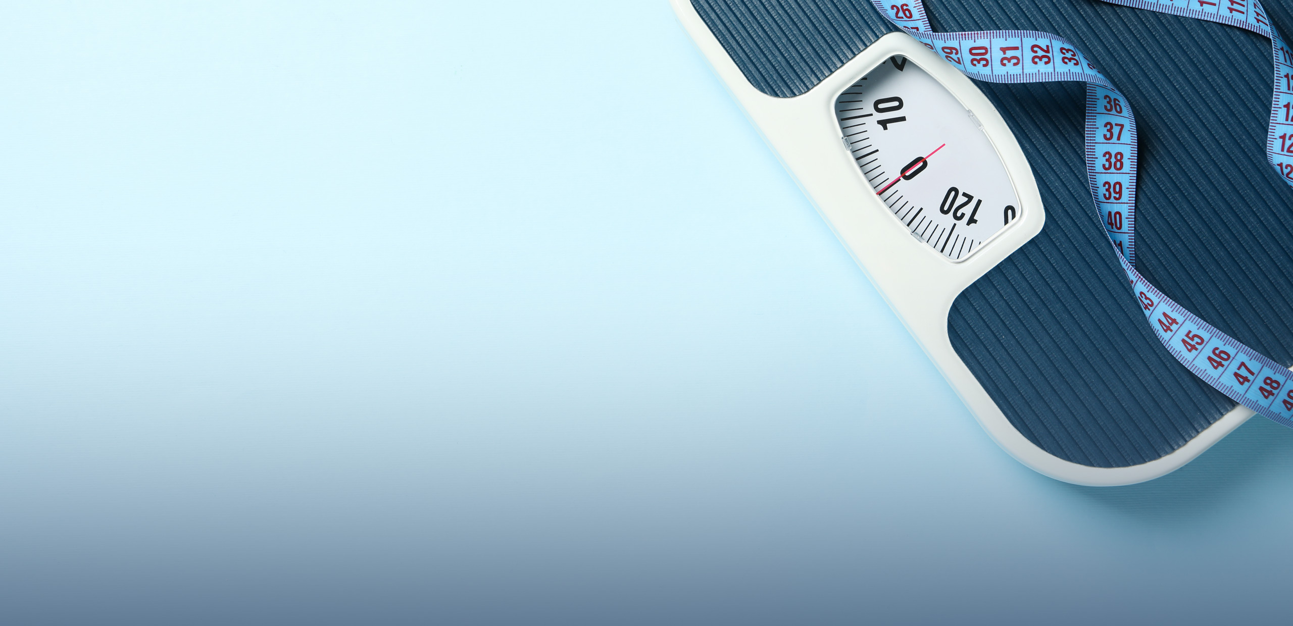 A top view of a mechanical bathroom scale with a white frame and dark blue ridged surface. The scale's needle points to zero, and a coiled blue measuring tape with red numbers is placed on the scale. The background is a smooth light blue gradient.
