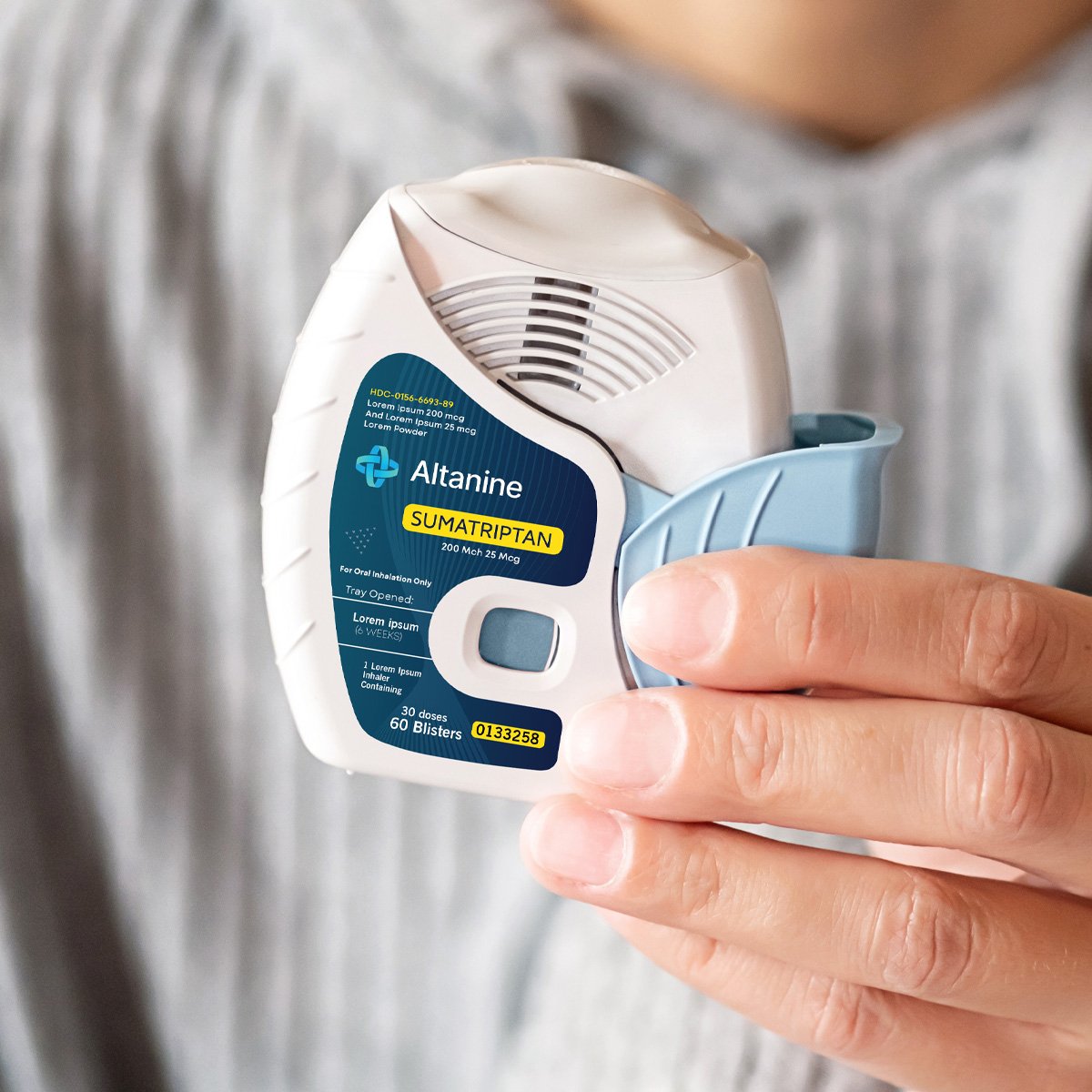Person holding an Altanine Sumatriptan inhalation device designed for migraine treatment. The white and light blue device features a labeled panel with dosage information (200 Mcg / 25 Mcg), brand logo, and product code 0133258.